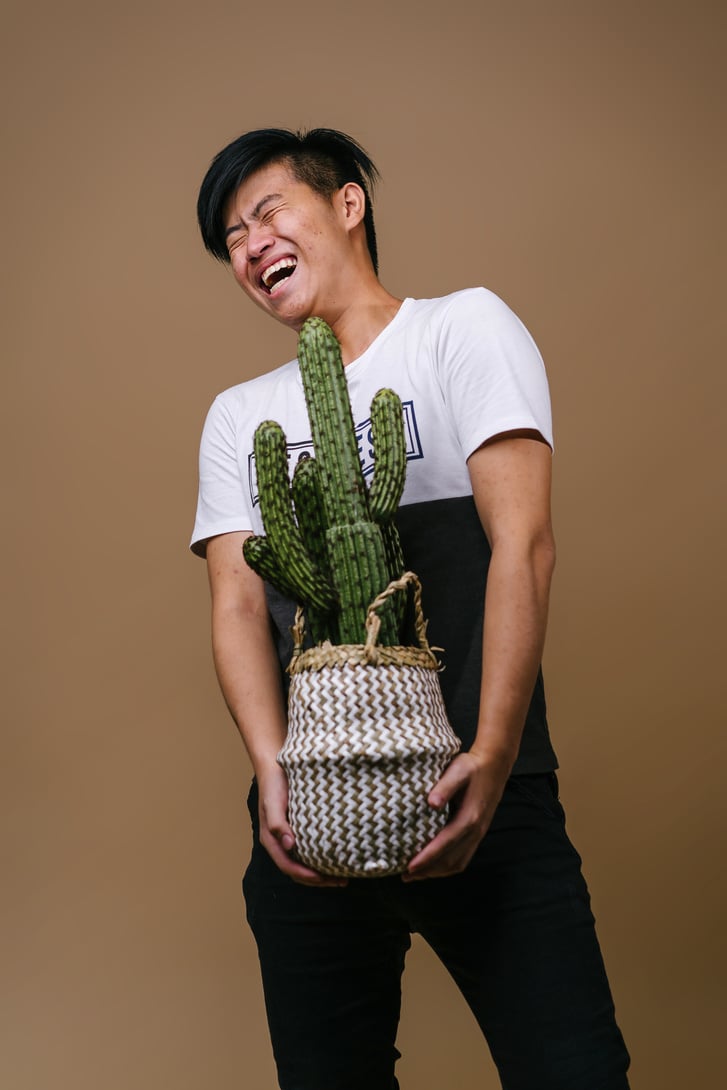 Man in White and Black Shirt Holding Pot With Cactus Plant